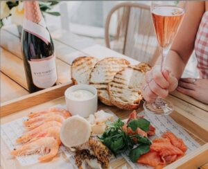 a woman holding a glass of Nyetimber Rosé wine at a table with a seafood platter on a wooden tray