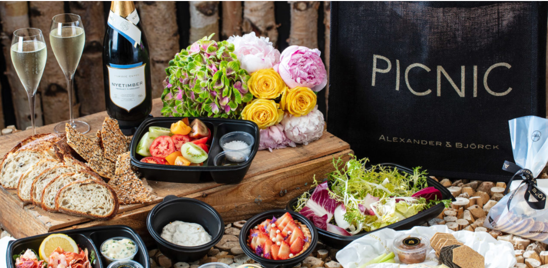 a full picnic spread including a Nyetimber Classic Cuvee wine bottle with two glasses, food containers and a bouquet of flowers