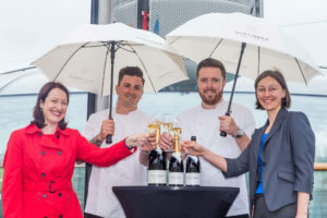 four people toasting wine glasses, holding umbrellas while at a sky bar
