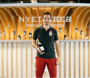 a man holding a bottle of Nyetimber wine in front of a wine bar with bottles presented behind it