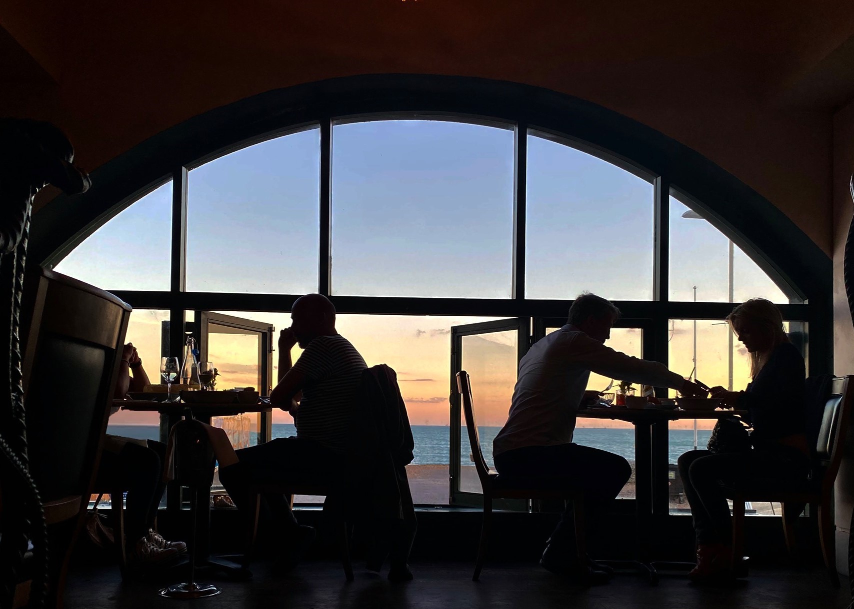 couples enjoying a glass of wine inside a restaurant that looks out over the sea and sunset