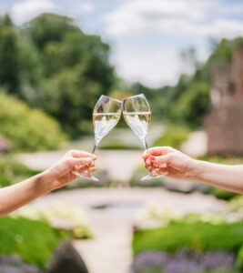 two people cheers their glass of wine in front of garden grounds