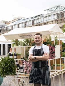 man stood in front of stall that contains wine bottles and flowers