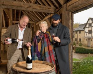 a man pouring wine while a woman and man enjoy a glass