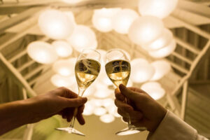 two wine glasses toasting under lights