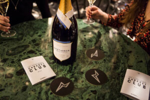 two people sat round a table in a lounge, wine bottle on table with coasters