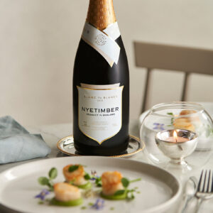 a table setting with a plate of food in front of a bottle of Nyetimber Blanc de Blancs wine and a lit candle