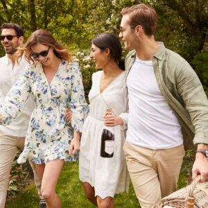 two couples walking in the forest laughing holding a bottle of Nyetimber wine and a picnic basket