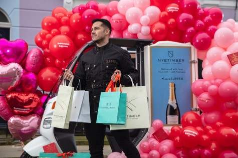 a man holding four luxury shopping bags in front of a red and pink balloon arch